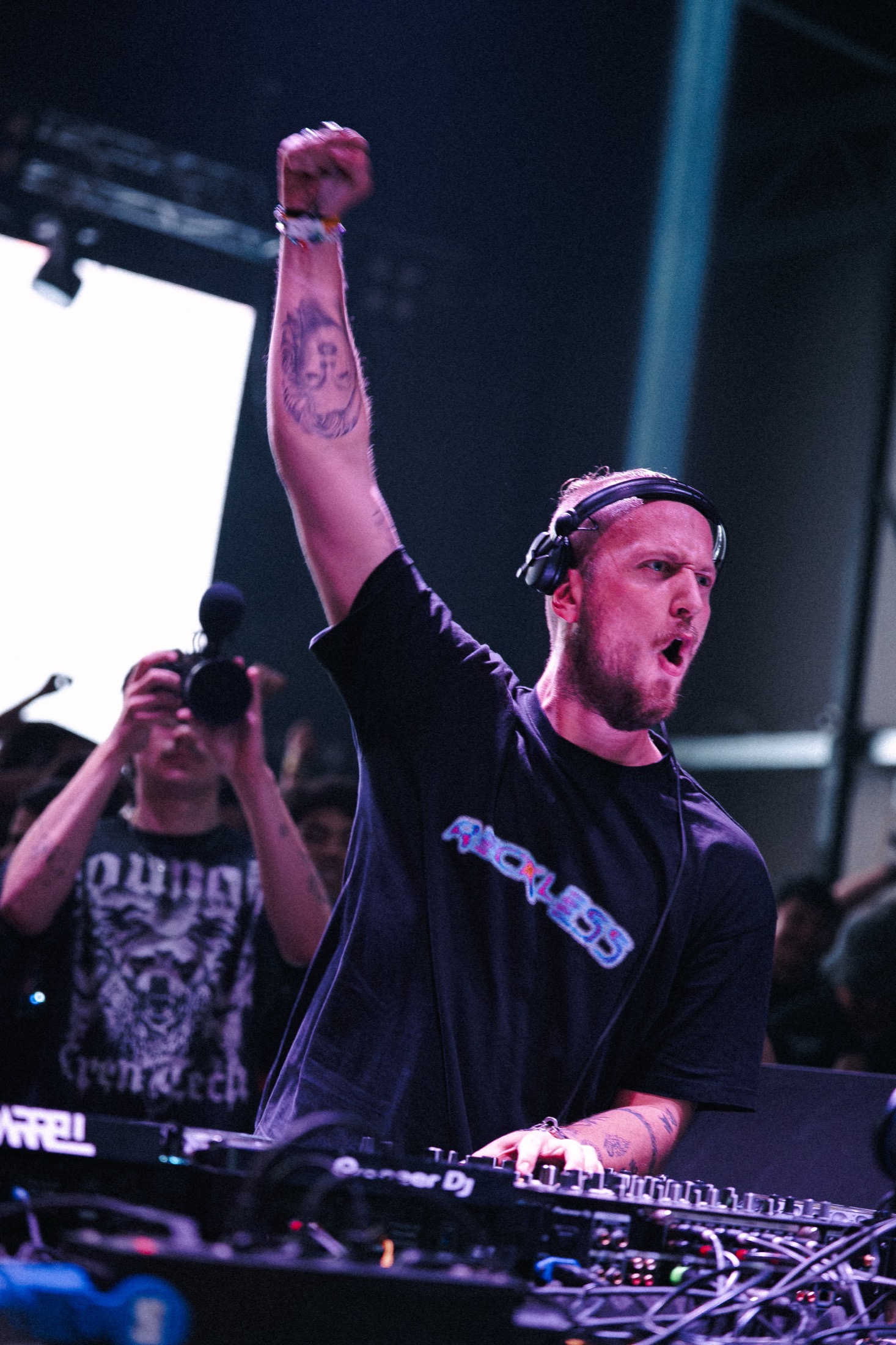 DJ con el puño en alto sobre la cabina, luces violeta y público al fondo — Libraphotos